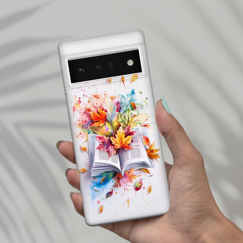 Op de afbeelding: Een witte telefoonhoes met een aquarelontwerp van een open boek met kleurrijke herfstbladeren. De bladeren zijn in tinten rood, oranje, geel en groen. Het boek is wit met zwarte tekst.