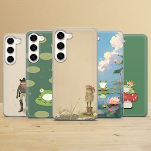 Pode incluir: Quatro capas de telefone diferentes com designs de sapos. As capas são transparentes e mostram a lente da câmera do telefone. Os designs incluem um sapo usando um chapéu de cowboy, um sapo sentado em um lírio d'água, um sapo usando um casaco e um chapéu, e um sapo usando uma coroa.