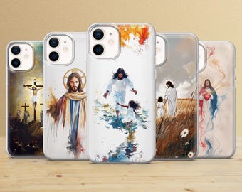 May include: Five clear smartphone cases featuring various watercolor-style religious illustrations of Jesus. The designs include scenes of the crucifixion, Jesus with a halo, walking on water with a child, walking through a field, and holding a heart.