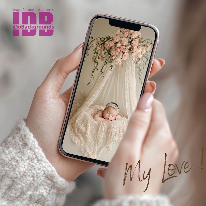 Puede incluir: Una persona sostiene un tel&eacute;fono inteligente que muestra una foto de un beb&eacute; durmiendo en una cuna de encaje blanco con un dosel floral. El texto "My Love!" est&aacute; escrito en la pantalla.