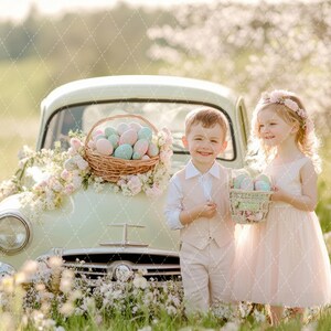May include: Two children, a boy and a girl, stand in front of a vintage car decorated with pastel Easter eggs and flowers. The girl is wearing a pink dress and a flower crown. The boy is wearing a light brown vest and pants. Both children are holding baskets of Easter eggs.