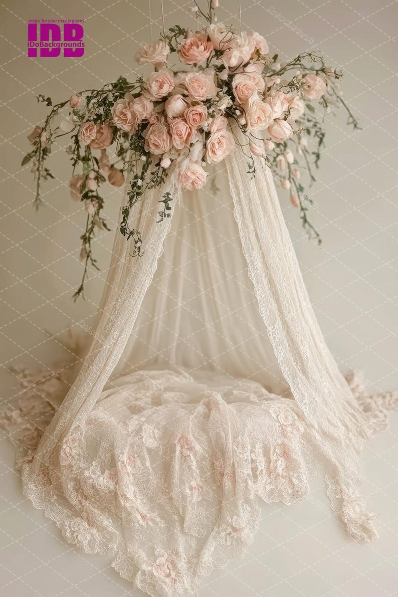 Puede incluir: Un dosel de encaje blanco con una guirnalda floral de rosas rosas que cuelga de la parte superior. El dosel est&aacute; drapeado sobre un coj&iacute;n de encaje blanco.