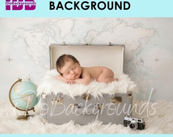 May include: A newborn baby lies peacefully on a fluffy white surface inside a gray suitcase. A vintage globe and camera are nearby. The background features a world map and the text "NEWBORN BACKGROUND". The logo "iDoBackgounds" is in the upper left corner.