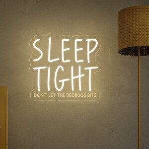 May include: White neon sign with the text "SLEEP TIGHT" and the phrase "DON'T LET THE BEDBUGS BITE" underneath. The sign is hanging on a grey wall in a bedroom setting.