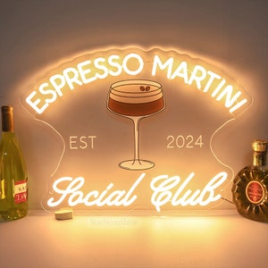 May include: White neon sign with the text "Espresso Martini Social Club" and the years "EST 2024". A stylized image of an espresso martini cocktail is in the center of the sign.