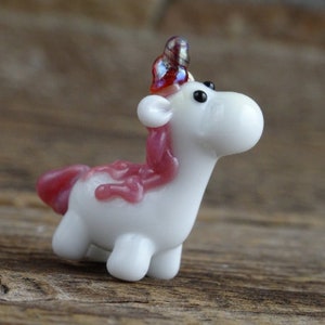 Op de afbeelding: Een klein wit glazen eenhoornbeeldje met een roze manen en staart. De eenhoorn heeft een rood en iriserend hoorn.