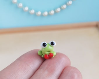 May include: A small green frog figurine with large black eyes and a red heart in its hands.