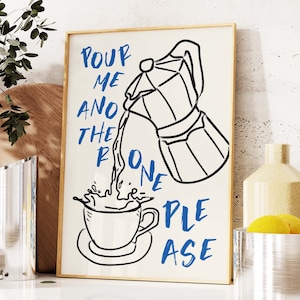 May include: A white framed print with a black and white illustration of a coffee pot pouring coffee into a cup. The text "POUR ME ANOTHER ONE PLEASE" is written in blue letters.