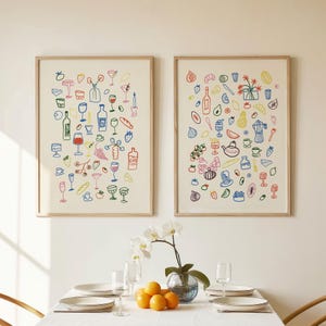 Puede incluir: Dos láminas enmarcadas con ilustraciones coloridas y caprichosas de alimentos y bebidas. Los dibujos incluyen botellas de vino, copas, frutas y otros elementos culinarios. Las láminas se exhiben sobre una mesa de comedor.