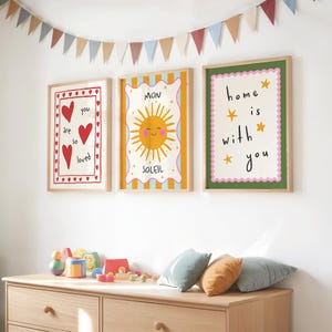 Puede incluir: Tres l&aacute;minas enmarcadas con mensajes positivos e ilustraciones. Una l&aacute;mina dice "you are so loved" con corazones rojos. Otra presenta un sol sonriente y la palabra "SOLEIL". La tercera dice "home is with you".