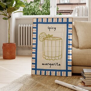 May include: A framed art print featuring a hand-drawn margarita cocktail illustration. The artwork includes the word "spicy" above the drink and "margarita" below. The frame has a blue and red border.