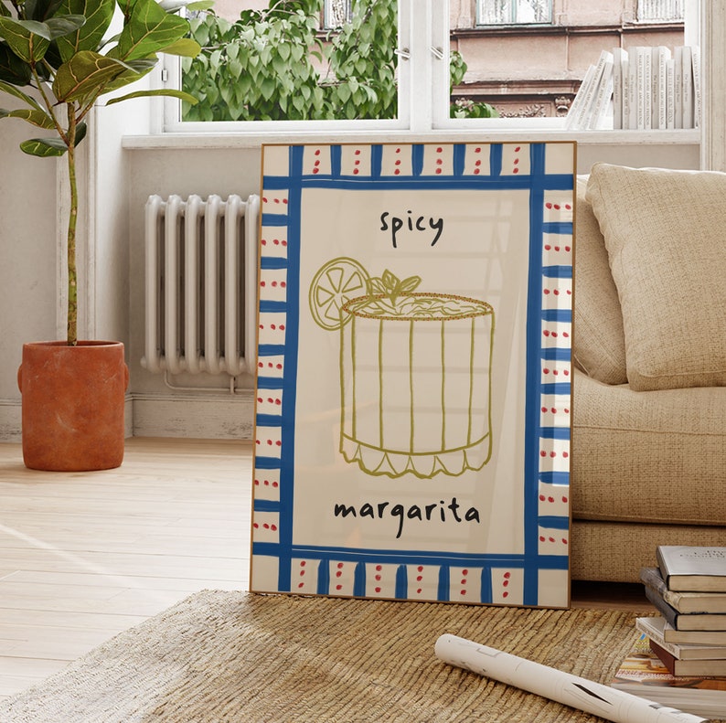 May include: A framed art print featuring a hand-drawn margarita cocktail illustration. The artwork includes the word "spicy" above the drink and "margarita" below. The frame has a blue and red border.