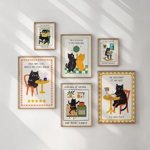 Op de afbeelding: Een verzameling ingelijste kunstprints met grillige illustraties van katten. Elke print heeft een uniek ontwerp met tekst, waaronder zinnen als "This Kitchen Is For Dancing" en "Un Croissant Et Un Café".