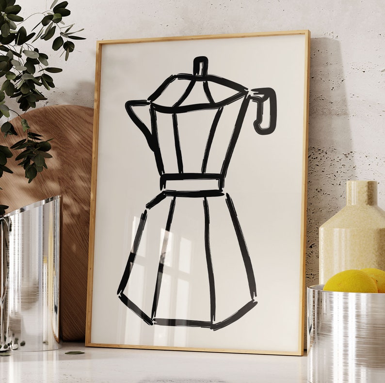 May include: A framed art print featuring a black line drawing of a stovetop espresso maker. The artwork is set against a cream-colored background and framed in a light wood. The image is a minimalist kitchen-themed illustration.