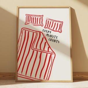 Pode incluir: Uma impressão emoldurada branca com um design listrado vermelho e branco. A impressão apresenta dois travesseiros listrados vermelho e branco e o texto "Every Minute Counts".