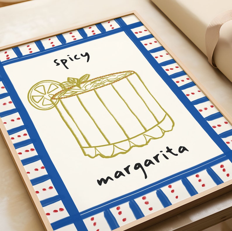 May include: A framed art print featuring a hand-drawn illustration of a spicy margarita cocktail. The artwork includes the words "spicy" and "margarita" in black script. The print has a blue and red border and a light wood frame.
