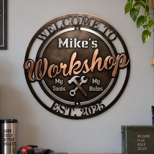 May include: A circular metal wall sign with a bronze finish featuring the text "Welcome to Mike's Workshop", "My Tools", "My Rules", and "Est. 2025". The design includes a central graphic of a crossed hammer and wrench, with bold lettering.