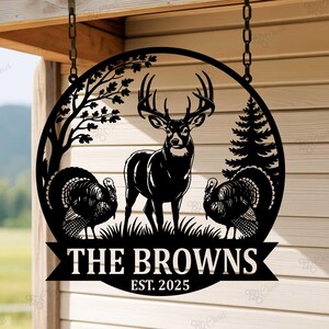 Puede incluir: Letrero de nombre familiar de metal negro con un ciervo, dos pavos, &aacute;rboles y el texto "THE BROWNS EST. 2025" en un dise&ntilde;o circular. El letrero est&aacute; colgado de una cadena.