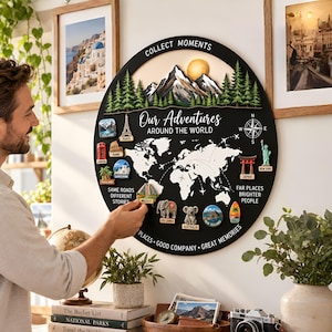 May include: A circular black wall plaque featuring a white world map, a mountain range, and the text "COLLECT MOMENTS", "Our Adventures AROUND THE WORLD", "SAME ROADS DIFFERENT STORIES", "FAR PLACES BRIGHTER PEOPLE", and "PLACES GOOD COMPANY GREAT MEMORIES".
