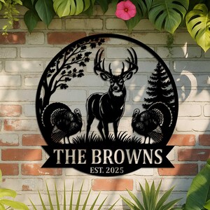 Puede incluir: Letrero de nombre familiar de metal negro con un ciervo, dos pavos y &aacute;rboles dentro de un marco circular. El letrero incluye el texto "THE BROWNS EST. 2025" en una pancarta. Est&aacute; montado en una pared de ladrillo.
