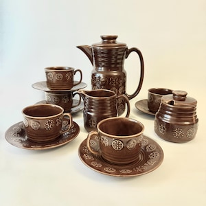 May include: A brown ceramic coffee set including a coffee pot, creamer, sugar bowl, cups, and saucers. The set has a decorative pattern of crosses and circles. The coffee pot is approximately 25 cm tall.