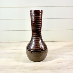 May include: A brown ceramic vase with a ribbed design. The vase has a narrow neck and a rounded base.