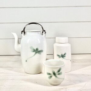 May include: A white ceramic tea set featuring a dragonfly design. The set includes a teapot, a small jug, and a teacup.