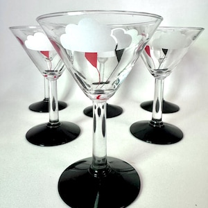 May include: A set of five martini glasses. Each glass has a black base and stem, with a clear bowl decorated with a white cloud design and red and black details. The glasses are displayed on a white surface.