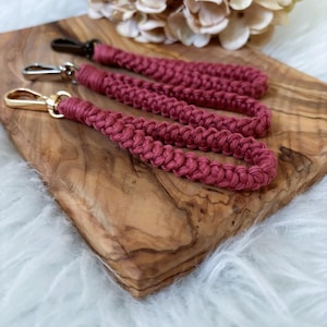 Könnte beinhalten: Drei geflochtene Schlüsselanhänger in Pink mit goldenen Metallverschlüssen auf einer Holzoberfläche.