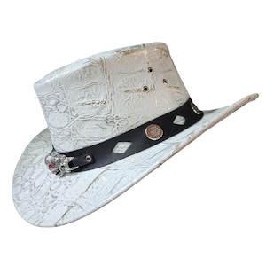 Może przedstawiać: Biały kowbojski kapelusz z czarną taśmą i srebrnymi akcentami. Kapelusz ma wzór w krokodyla i klamrę w kształcie czaszki.