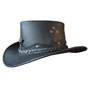 Könnte beinhalten: Ein schwarzer Cowboyhut aus Leder mit einem geflochtenen Band, silbernen Nieten und einem silbernen Schlüsselloch-Design. Der Hut hat eine breite Krempe und eine hohe Krone.