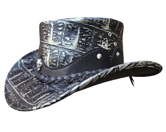 May include: A black and white cowboy hat with a braided leather band and silver accents. The hat has a textured, crocodile-like pattern.