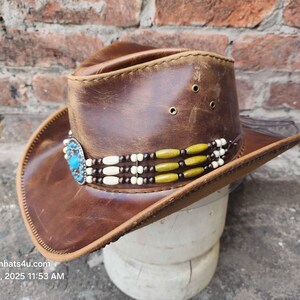 May include: A brown leather cowboy hat with a turquoise and silver concho and a beaded band with white and green beads.