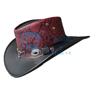 Könnte beinhalten: Ein Cowboyhut mit einem rot-schwarzen Schlangenledermuster auf der Krone und einer einfarbig schwarzen Krempe. Der Hut verfügt über ein dekoratives Band mit einem silberfarbenen Stierschädel-Emblem und einem strukturierten ovalen Akzent.
