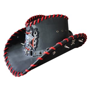 Könnte beinhalten: Schwarzer Leder-Cowboyhut mit roten Nähten und einem Totenkopf- und Flammen-Design. Der Hut hat Metallnieten am Rand.