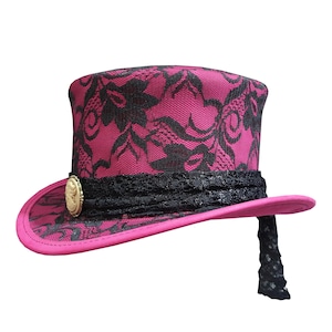 Könnte beinhalten: Ein rosa Zylinder mit schwarzem Spitzenmuster und goldener Verzierung. Der Hut hat ein schwarzes Band und einen schwarzen Spitzenbesatz.