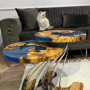 K&ouml;nnte beinhalten: Zwei runde Holz-Couchtische mit blauen Harzeinlagen. Die Tische sind &uuml;bereinander gestapelt und haben ein einzigartiges, modernes Design mit einem Edelstahlfu&szlig;.