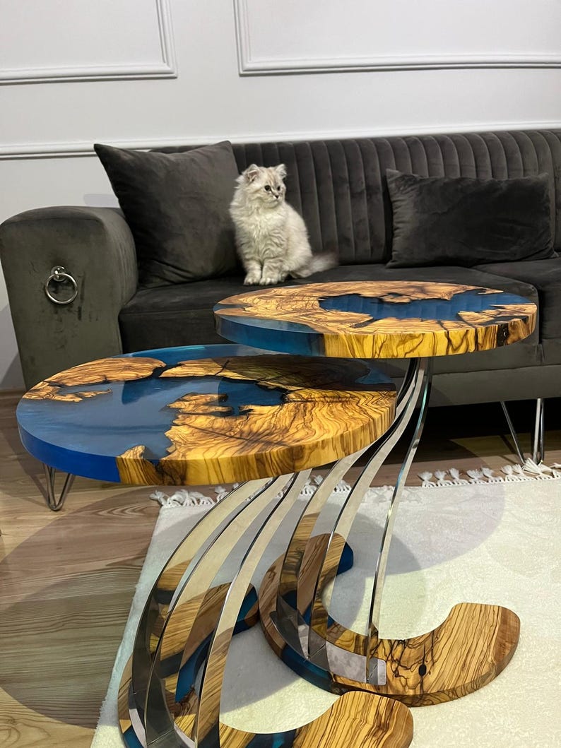 K&ouml;nnte beinhalten: Zwei runde Holz-Couchtische mit blauen Harzeinlagen. Die Tische sind &uuml;bereinander gestapelt und haben ein einzigartiges, modernes Design mit einem Edelstahlfu&szlig;.