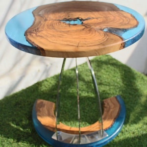 K&ouml;nnte beinhalten: Ein runder Holztisch mit einer blauen Epoxidharzplatte und einem silbernen Metallfu&szlig;. Der Tisch steht auf einer gr&uuml;nen Grasfl&auml;che.