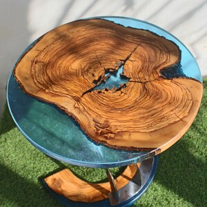 K&ouml;nnte beinhalten: Eine runde Tischplatte aus Holz mit einer blauen Epoxidharzeinlage. Der Tisch hat ein Metallgestell mit einem einzigartigen Design.