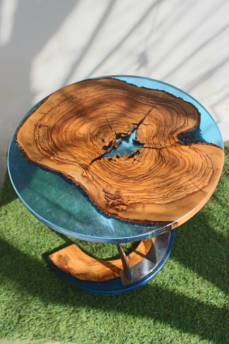 K&ouml;nnte beinhalten: Eine runde Tischplatte aus Holz mit einer blauen Epoxidharzeinlage. Der Tisch hat ein Metallgestell mit einem einzigartigen Design.