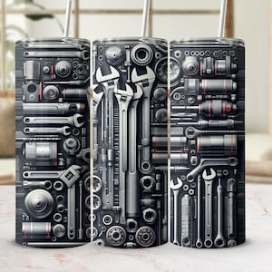 Puede incluir: Tres vasos de acero inoxidable con un diseño negro y plateado que presenta varias herramientas y herrajes. Los vasos son una excelente manera de mantener tus bebidas frías o calientes.