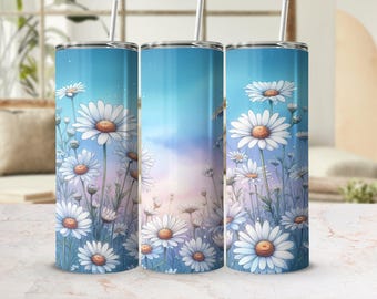 Puede incluir: Tres vasos de acero inoxidable con un diseño floral. Los vasos presentan un fondo degradado azul, rosa y blanco con un patrón de margaritas blancas y hojas verdes.
