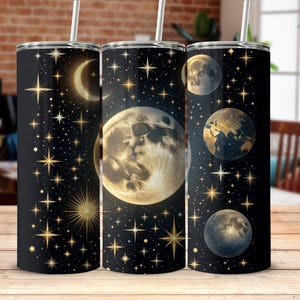 Pode incluir: Três copos de aço inoxidável com fundo preto e desenhos celestiais dourados. Os desenhos incluem estrelas, luas e planetas.