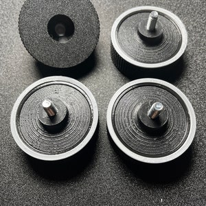 Op de afbeelding: Vier zwarte kunststof camera-statiefbevestigingen met een zilveren ring rond de rand. Drie van de bevestigingen hebben een schroefdraad in het midden.