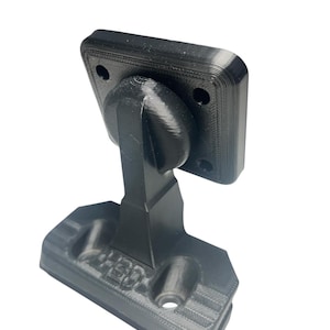 Puede incluir: Soporte negro impreso en 3D con una sección superior rectangular con dos agujeros. El soporte tiene una rótula y una base con el texto "1-30" en relieve. El objeto está diseñado para el montaje.