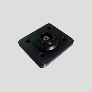 Op de afbeelding: Zwarte 3D-geprinte houder van plastic met een gouden schroef met schroefdraad in het midden.