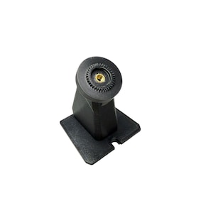 May include: A black, angled mount with a circular top featuring a gold-colored center. The mount is attached to a square base with a small cutout. The object is made of a textured material.
