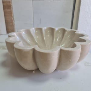 May include: A large, white, marble bowl with a scalloped edge. The bowl is shaped like a flower and has a smooth, polished surface.