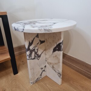May include: A round white marble side table with a unique, veined pattern. The table has a circular top and a base with a geometric design.